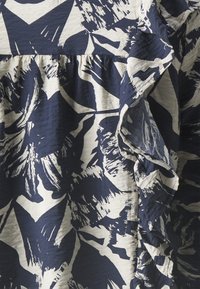 Tessuto a fantasia blu navy e bianco con disegni astratti simili a foglie, bordi arricciati e un materiale leggero e testurizzato.