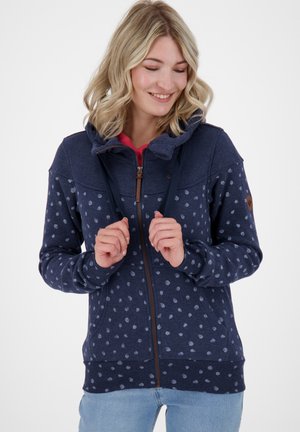 Navy blauwe zip-up hoodie met lichtblauwe stippen, een trekkoordkap, voorzakken en een bruine ritsaccent. Zachte stoftextuur.