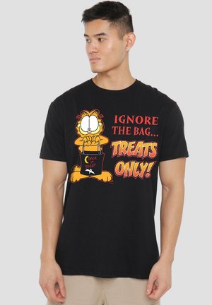 Mann trägt ein schwarzes T-Shirt mit Garfield, der eine Süßigkeiten-Tüte hält, und dem Text "Ignoriere die Tüte... Nur Süßigkeiten!" in Halloween-Schriftart.