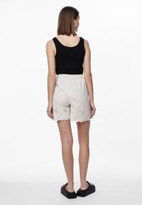 Čierny top bez rukávov skombinovaný s svetlo béžovými šortkami s vyšívaním na leme. Modelka má na sebe čierne platformové sandále.