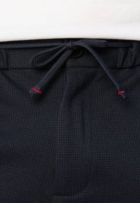 Granatowe spodenki z teksturowanej tkaniny, z sznurkiem w pasie ozdobionym czerwonymi akcentami oraz zapięciem na guzik.