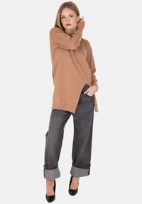 Maglione lungo a maniche fluttuanti color marrone chiaro con fessure laterali, abbinato a jeans larghi grigio scuro con risvoltini e tacchi alti neri.