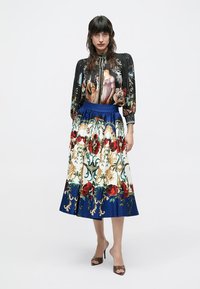 Camicia stampata con base nera caratterizzata da illustrazioni dettagliate; gonna al ginocchio bianca e blu con motivi floreali e vita elasticizzata.