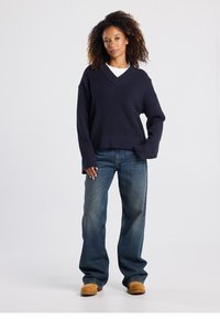 Navy ribbed knit sweater with a V-neck, paired with light blue wide-leg jeans and tan footwear, showcasing a relaxed fit and texture.