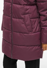Bordo puffer kaput s vertikalnim kvadratima, s bočnom džepom i zatvaranjem na patentni zatvarač. Glatka, lagana tkanina.