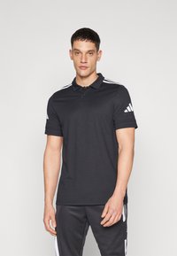 Svart polo skjorte med krage og tre-knappers placket. Har hvite striper på skuldrene. Stoffet ser glatt og lett ut.