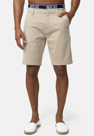 Beige shorts i struktureret stof, med knaplukning, frontlommer og en blå mærkebånd i taljen. Kantene er foldet.