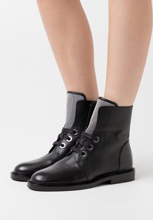 Czarne skórzane botki na kostkę mają strukturalne wykończenie, szare elastyczne wstawki oraz czarne sznurowadła z srebrnymi oczkami. Płaska prostokątna podeszwa.