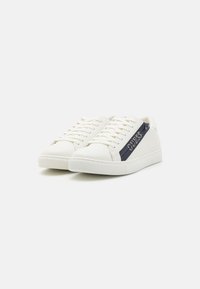 Sneaker bianche realizzate in materiale sintetico, con una striscia blu navy con il logo "GUESS", suola bianca piatta e design classico con lacci.