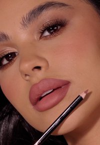 Zbliżenie twarzy osoby z pełnymi, matowymi, mauve'owymi ustami i wyostrzonym ołówkiem do ust. Skóra promienna, z wyraźnie zarysowanymi brwiami i neutralnym cieniem do powiek.