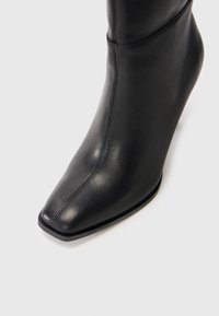 Black leather ankle boot with a pointed toe, smooth texture, and minimal stitching details. Features a sleek, fitted design.
