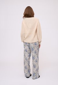 Pull en tricot beige avec une coupe décontractée, associé à un pantalon gris clair à motifs floraux bleus et verts. Chaussures plates.