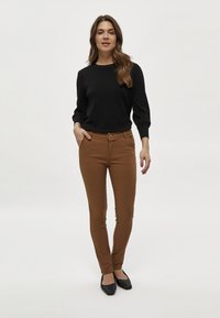 Svart tröja med långa ärmar, slim-fit bruna byxor och svarta mönstrade ballerina skor. Slät tyg och skräddarsydd design.