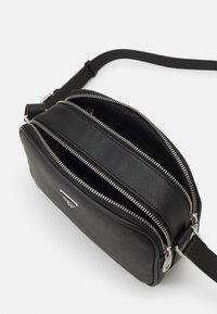 Borsa a tracolla in pelle nera con due scomparti con zip e dettagli in metallo argentato. Presenta una finitura testurizzata e una tracolla regolabile.