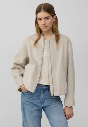 Hellbeige, kurz geschnittene Jacke mit Reißverschluss, ausgestattet mit einem runden Halsausschnitt und leicht übergroßen Ärmeln, kombiniert mit einem gestreiften Oberteil und Jeans.