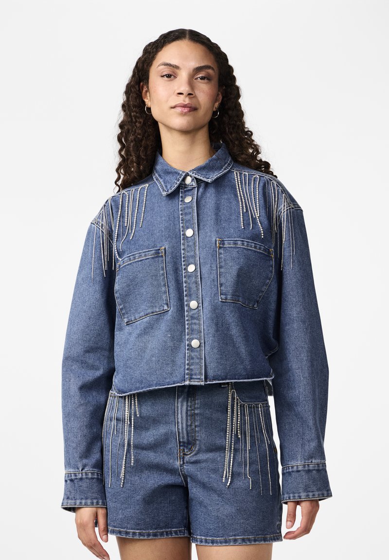 Denim lühike jakk, millel on kraega kaelus, hõbedased frantsi aksessuaarid õlgadel, kaks esist pocketit ja nupuga sulgemine.