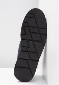 Semelle de chaussure en caoutchouc noir avec un motif de bande de roulement géométrique, présentant une légère courbure et une surface texturée. Conception légère et durable.