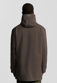 Bruine met een capuchon gevoerde jas met een gladde textuur, een volledige lengte en verstelbare manchetten; heeft een label bij de kraag en geen zichtbare sluitingen.