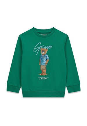 Groen sweatshirt met lange mouwen met een afbeelding van een beer die een blauw shirt, beige korte broek en sandalen draagt, met de tekst "Guess" erboven.