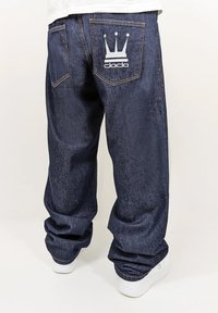 Dark blue denim jeans with a relaxed fit, featuring a white crown logo and "dada" text on the back pocket. Visible stitching detail.