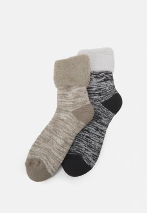 Twee paar sokken: de ene in beige met een pluche manchette en gestreept ontwerp, de andere in grijs met een gestructureerd patroon en een zwarte teen.