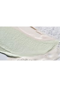 Romige witte en zachte groene textuurproducten vermengen zich met witte bubbels, waardoor een soepele visuele contrast op een lichte achtergrond ontstaat.