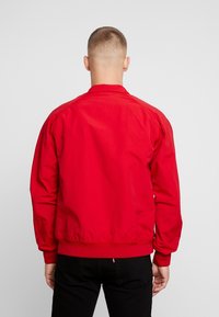 Röd bomberjacka med ribbade ärmslut och nederkant, tillverkad av ett mjukt, lättviktigt tyg och med en enkel, odekorerad design.
