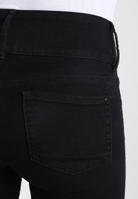 Vaqueros de mezclilla negra con un diseño ajustado, que presentan bolsillos traseros estándar, una textura suave y detalles de costura mínimos.