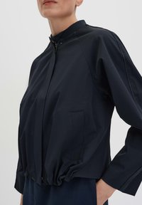 Navy blue bomber jacket with a high collar, elastic waist, and zip closure. Features long sleeves and side pockets for added utility.