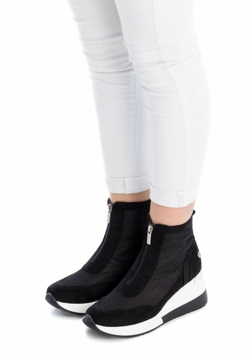 Botas negras hasta el tobillo con paneles de malla, cremalleras laterales y suelas de cuña blancas. El diseño presenta una parte superior texturizada en negro y una punta lisa.