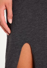 Grå mjuk tyg med en sidospricka, med en närbild av en hand som vilar på materialet och framhäver textur och rörelse.