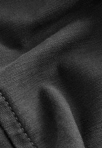 Gros plan d’un tissu noir tissé avec texture visible, coutures et plis doux créant des contrastes de lumière et d’ombre.