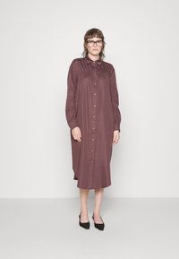 Vestido de manga longa, com botões, na cor mauve profundo, feito de tecido suave. Apresenta detalhes franzidos nos ombros e uma bainha curva.