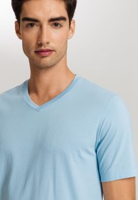 Camiseta de pico azul claro hecha de algodón suave. Presenta mangas cortas y una textura lisa. Diseño simple sin patrones ni adornos.