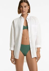 Vit linneskjorta med avslappnad passform och uppvikt ärm, kombinerad med en grön texturerad bikiniöverdel och matchande underdel.