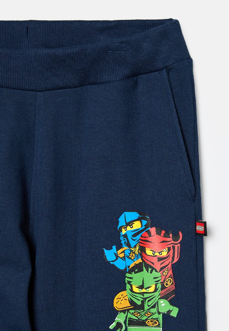 Marineblaue Sweatpants aus weichem Stoff, mit einem bunten Grafikdesign von drei Ninja-Charakteren. Enthält ein kleines LEGO-Tag an der Seite.