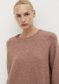 Light pink knit sweater with a ribbed crew neckline, featuring a relaxed fit and subtle texture details in the fabric.