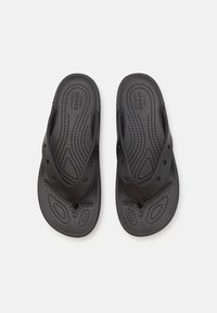 Tongs noires en caoutchouc avec un lit de pied texturé, des points surélevés pour une meilleure adhérence, et des lanières étroites en forme de V.
