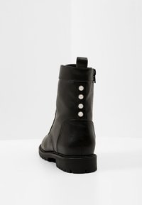 Černé kotníkové boty vyrobené z kůže, s designem kulaté špičky, texturovanými boky a čtyřmi perlovými detaily na zadní straně. Zapínání na zip.