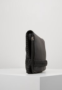Borsa a mano nera in pelle con superficie texture, caratterizzata da dettagli intrecciati lungo la cerniera e una forma rettangolare elegante.