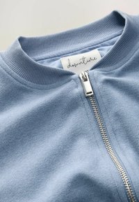 Blue zip-up sweatshirt made of soft, textured fabric with ribbed collar and a silver zipper. Label attached inside reads "downtime."