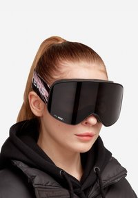 Gafas de esquí con un diseño de lente oscura y grande, que presentan un marco negro suave y una correa de patrón rosa etiquetada "LUX by ZEISS."