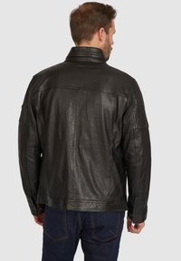 Schwarze Lederjacke mit hohem Kragen, strukturiertem Rücken und detaillierten Nähten. Kombiniert mit dunkelblauen Jeans, von hinten betrachtet.