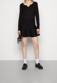 Top negro de manga larga con costillas y escote en V, combinado con una falda negra acampanada. Los accesorios incluyen un bolso de mano con estampado de cebra y zapatos negros.