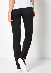 Zwarte skinny jeans van gestructureerde stof, met twee achterzakken en een slim fit. Gecombineerd met zwarte instappers met witte zolen.