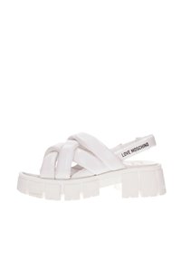 Sandalias de plataforma blancas con un diseño superior anudado en material brillante, con suela gruesa y una correa de marca en la parte trasera.
