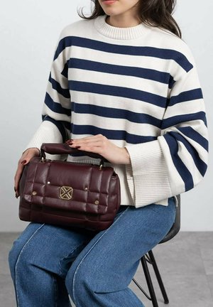 Bolso de piel burdeos con diseño acolchado, herrajes dorados y un asa superior. Se lleva un suéter de punto a rayas y jeans azules.