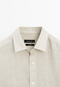 Beige linen button-up shirt with a pointed collar and subtle vertical stripes, featuring a black label inside the collar.