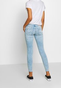 Jeans skinny de denim azul claro con una textura desgastada, con una cinturilla de altura media y bolsillos traseros, combinados con zapatos negros tipo slip-on.