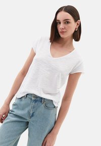Witte v-hals t-shirt van lichtgewicht stof, met korte mouwen en een relaxte pasvorm, gecombineerd met high-waisted lichtblauwe jeans.
